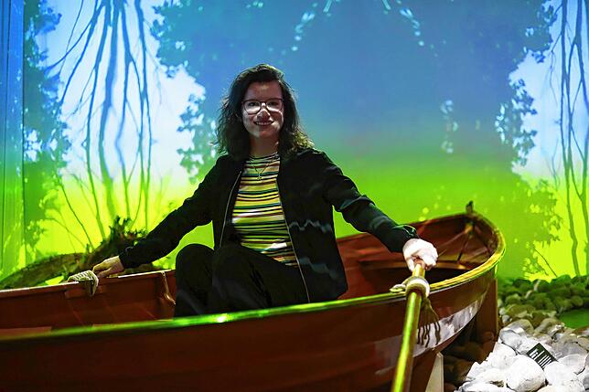 Anthea Befurt sitzt in einem Ruderboot, rings um sie die virtuelle Darstellung des Bodensees bei Nacht. Besucher der Ausstellung zum ...