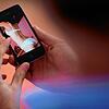 Das Symbolfoto zeigt einen jungen Mann, der auf ein Smartphone schaut, auf dem ein erotisches Foto einer jungen erwachsenen Frau zu ...