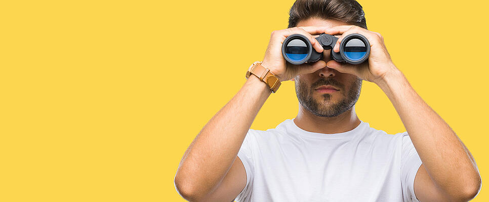 Young handsome man looking through binoculars over isolated background with a confident expression on smart face thinking serious