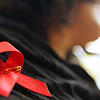 Eine Frau hat sich eine rote Schleife angeheftet. Die Schleife ist ein Symbol der Solidarität mit Menschen, die Aids haben oder ...