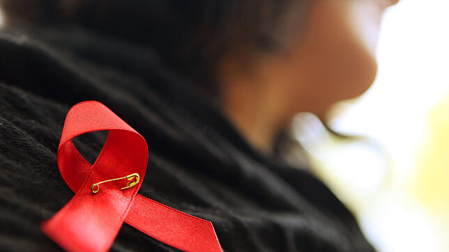 Eine Frau hat sich eine rote Schleife angeheftet. Die Schleife ist ein Symbol der Solidarität mit Menschen, die Aids haben oder ...