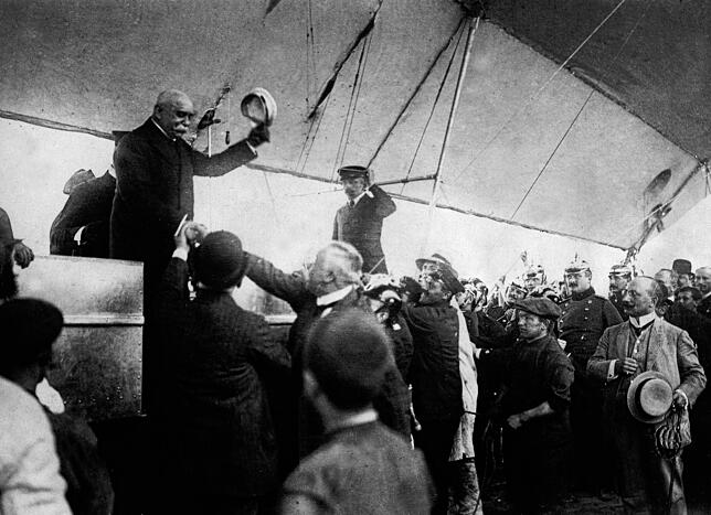 Ferdinand Graf Zeppelin, der seine Mütze lüftet, wird bei seiner Luftschiff-Ankunft in Düsseldorf begrüßt.