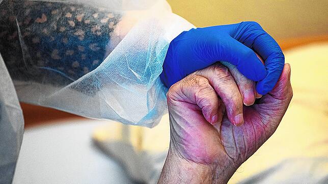 Eine Altenpflegerin in Schutzausrüstung hält die Hand eines Heimbewohners. (Symbolbild)