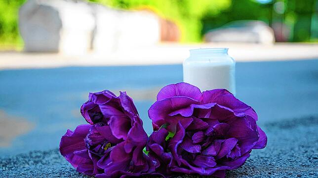 Blumen und eine Kerze liegen auf einem Schotterplatz vor dem Eingang zu einem Spielplatz. Auf einem Spielplatz im Sauerland soll in der ...