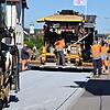 Ein Fertiger (hinten) bringt Asphalt und das spezielle Abtreumaterial, das zur Reinheit der Luft beiträgt und den Lärm reduziert, auf. ...