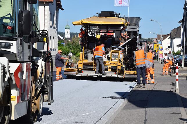 Ein Fertiger (hinten) bringt Asphalt und das spezielle Abtreumaterial, das zur Reinheit der Luft beiträgt und den Lärm reduziert, auf. ...