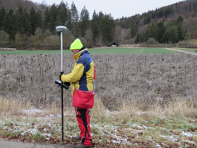 Thomas Stickel von der Firma Bit-Ingenieure bei der Geländeaufnahme für den Neubau, der auf dem Rapsacker im Hintergrund vor dem Wald ...