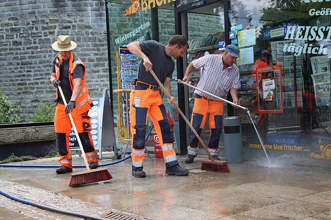 Mit Wasserschlauch und Besen gehen René Stipp, Rainer Längle und Thomas Schäfer gehen am Bahnhof gegen den Schlamm vor.