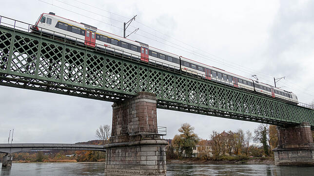 Ein Zug überquert die historische Eisenbahnbrücke zwischen Waldshut und Koblenz, fotografiert vom Schweizer Rheinufer aus.
