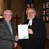 Pfarrer Peter Krech (rechts) gratuliert Harald Apelt zur Verleihung der goldenen Ehrennadel der evangelischen Landeskirche Baden und ...