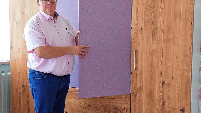 Gebhard Herrmann demonstriert einen Schlafzimmerschrank aus Eichenholz. Die Türen sind mit Stoff bezogen.