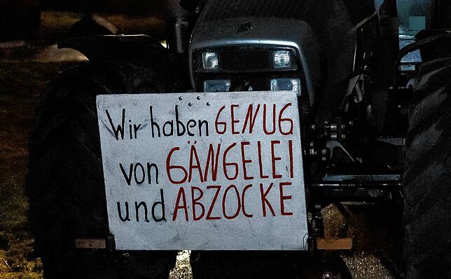 „Wir haben genug von Gängelei und Abzocke“, steht auf einem Protestplakat am Rande des Mahnfeuer-Treffens von Landwirten im ...