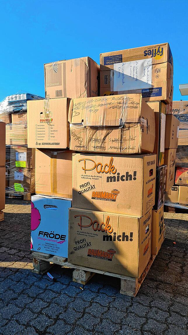 Paletten mit Babynahrung, Windeln, Decken, Kleidern und Hygieneartikeln stehen auf dem Parkplatz.
