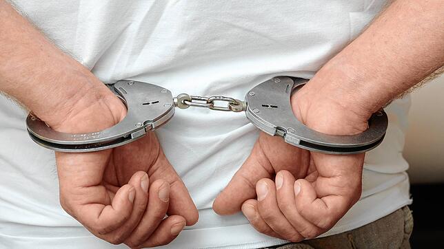 Zwei männliche Hände sind auf diesem Symbolfoto in Polizeihandschellen gefesselt.