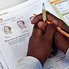 Ein Lehrbuch liegt in einem Deutschkurs für Flüchtlinge vor einem jungen Mann auf der Schulbank. Im Landkreis müssen Flüchtlinge lange ...