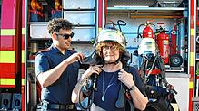 Ganz schön schwer: Grünen-Stadträtin Annette Hufschmidt bekommt Teile einer Feuerwehrausrüstung für den Atemschutz angelegt.