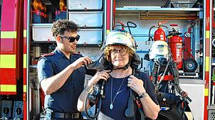 Ganz schön schwer: Grünen-Stadträtin Annette Hufschmidt bekommt Teile einer Feuerwehrausrüstung für den Atemschutz angelegt.