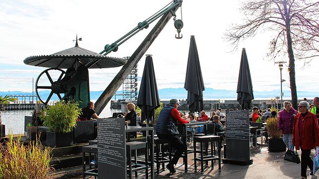 Um den Hafenkran herum sind Stühle und Tische eines Restaurants aufgestellt. Im Hintergrund ist der Moleturm zu sehen.