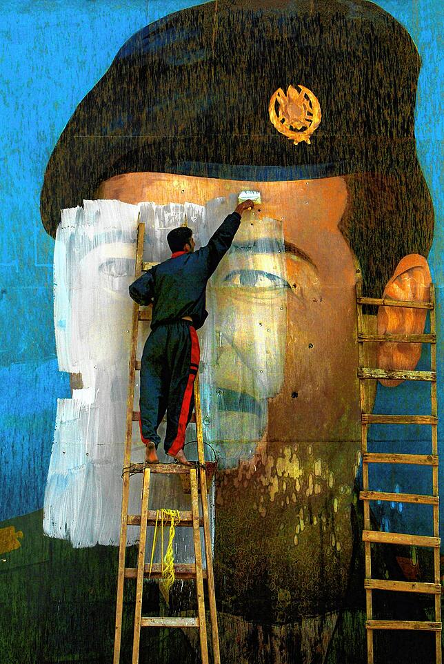 Ein Iraker übermalt nach dem Sturz Saddam Husseins ein von Einschüssen durchlöchertes Porträt – eingefangen von Carolyn Cole.