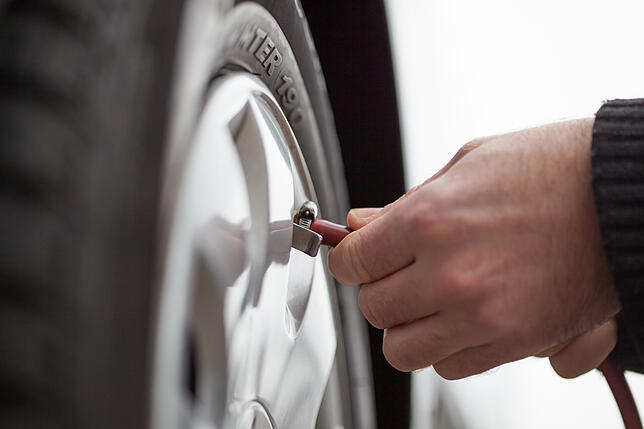 Ein Autofahrer pumpt einen Autoreifen auf: Ein niedriger Reifenluftdruck wirkt sich auf den Spritverbrauch aus.