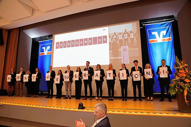Mitarbeiter der Volksbank zeigen am Ende der Vertreterversammlung den Slogan „Next Generation“