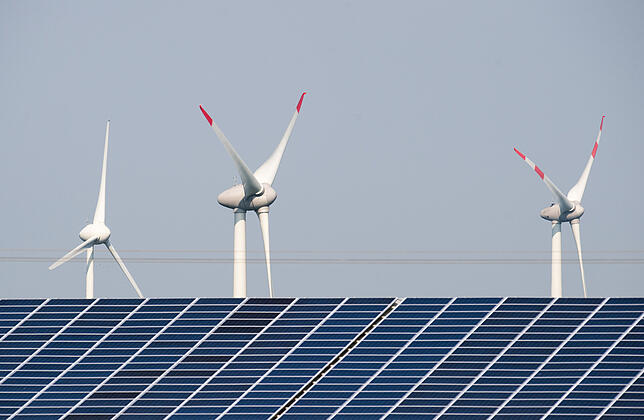 Windräder, die sich in Schleswig-Holstein hinter einer Solaranlage drehen. Fluktuierende Einspeisung von Strom belastet die Netze.