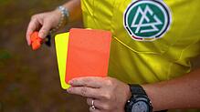 Unser Symbolbild zeigt eine Schiedsrichterin, die mit der Roten und Gelben Karte auf einem Rasen steht.