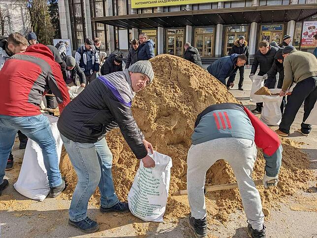 Freiwillige Helfer befüllen Sandsäcke, um Straßenblockaden für Panzer zu errichten.