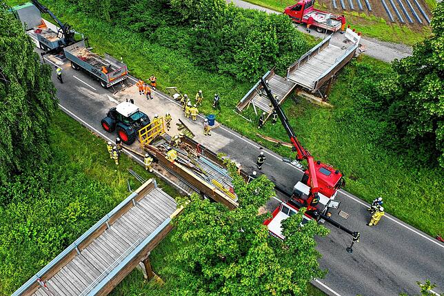 Die Feuerwehr Meckenbeuren hebt mit einem Kran einen Teil der zerstörten Brücke an.