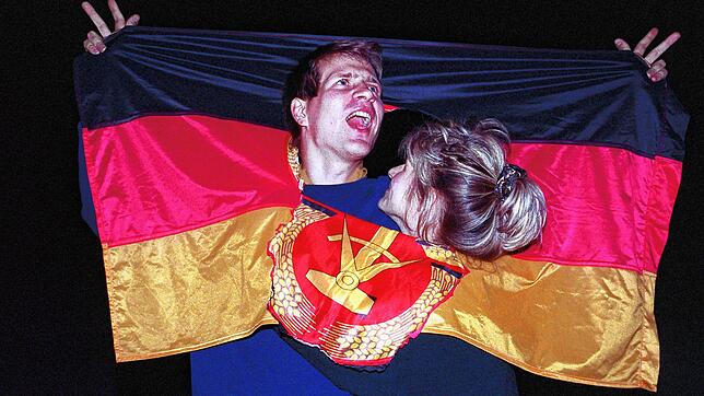 Ein jubelndes Paar hat sich am Tag der Deutschen Einheit 1990 am in einer DDR-Fahne dort Platz geschaffen, wo früher das Emblem Hammer ...