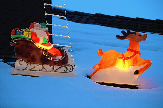 Auf dem Dach zieht ein Rentier den Schlitten des Weihnachtsmannes durch den Schnee – natürlich beleuchtet.