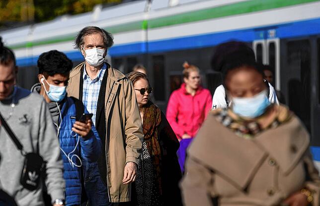 Fahrgäste am Bahnhof tragen Gesichtsmasken. In Ländern, in denen Maskenpflicht herrscht, gibt es deutlich weniger schwere Erkrankungen. ...