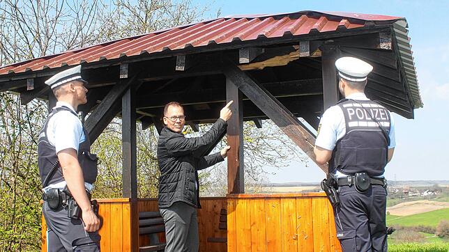 Bürgermeister Thorsten Scigliano (Mitte) begutachtet mit zwei Polizisten den Schaden an der Hütte.