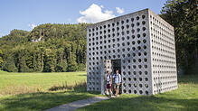 SÜDKURIER-Mitarbeiter Katja Huber und Yannick Peter vor einem durchlöcherten Kubus mitten auf einer grünen Wiese. Das Wasserhaus St. ...