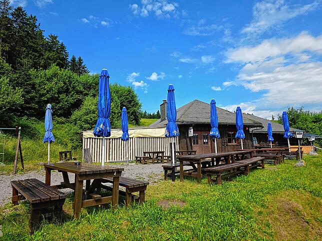 Der Außenbereich vor dem „Ackerloch Grillschopf“: Rustikale Holzgarnituren laden zum Verweilen und zum Blick in die Ferne.