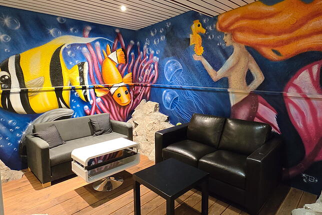 Die farbenfrohe Wandgestaltung rührt noch aus Zeiten des Hallenbades. Jetzt laden hier Sofas zum Verweilen ein.