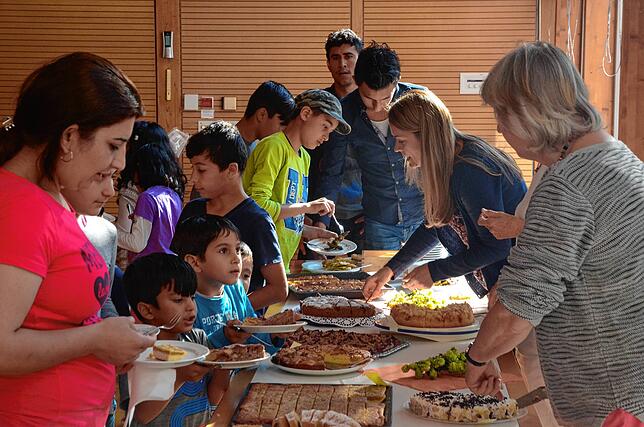 Irmgard Teske und Christin Jungblut vom Mehrgenerationenhaus teilen an der Tafel im Café International Kuchen aus.