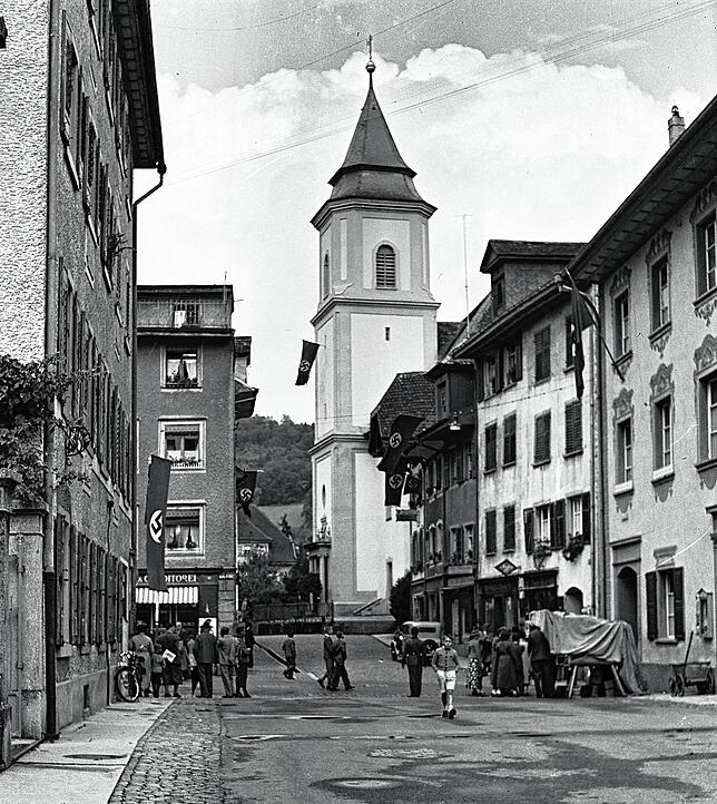 Die Waldshuter Marienstraße mit Hakenkreuzbeflaggung, im Hintergrund die Kirche sowie einige Passanten und Kinder.