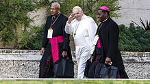 Papst Franziskus (Mitte) geht mit zwei Bischöfen durch die Vatikanstadt.