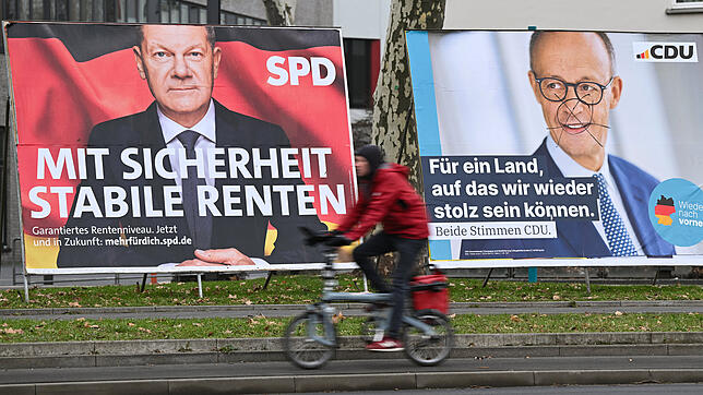 Ein Radfahrer fährt im Frankfurter Osten an zwei Wahlplakaten mit den Spitzenkandidaten von SPD und Union, Kanzler Olaf Scholz (l) und ...
