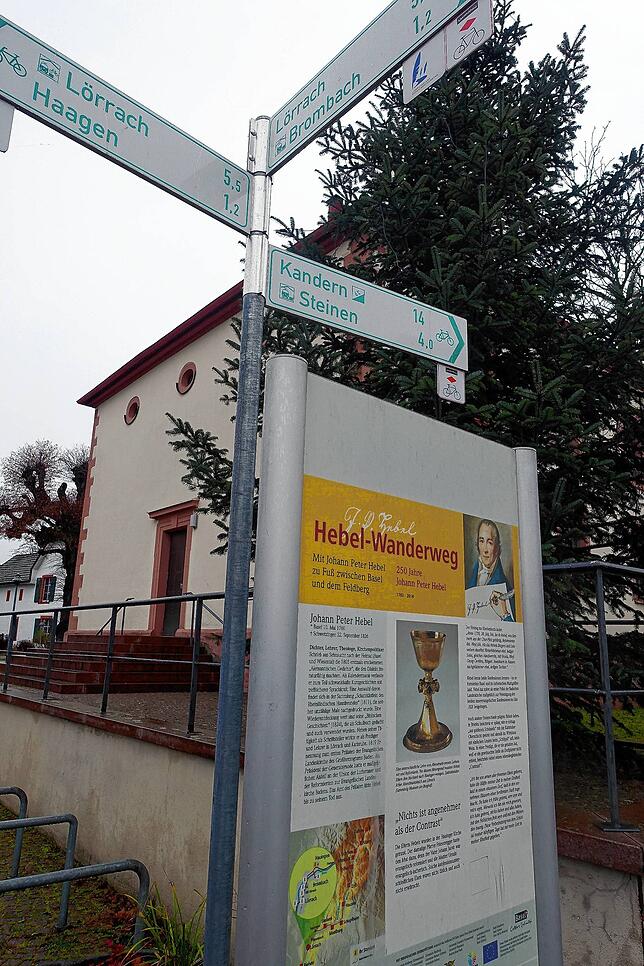 Infotafeln säumen den Hebel-Wanderweg, hier eine Stele vor der Kirche mit Weihnachtsbaum in Lörrach-Hauingen, wo Hebels Eltern getraut ...