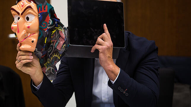 Der Angeklagte hält im Amtsgericht Heilbronn eine Hexenmaske hoch.