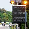 Reisende aus Risikogebieten mit einer Leuchttafel &bdquo;Rückreise aus Risikogebiet? Quarantäne einhalten!&ldquo; auf die notwendigen ...