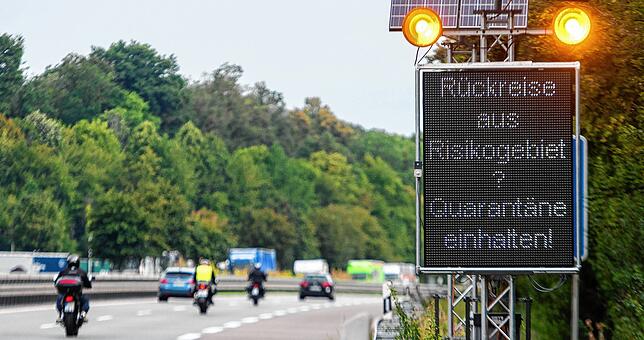 Reisende aus Risikogebieten mit einer Leuchttafel „Rückreise aus Risikogebiet? Quarantäne einhalten!“ auf die notwendigen ...