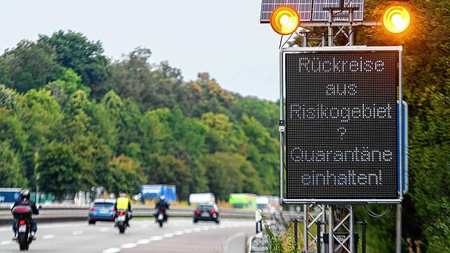 Reisende aus Risikogebieten mit einer Leuchttafel &bdquo;Rückreise aus Risikogebiet? Quarantäne einhalten!&ldquo; auf die notwendigen ...