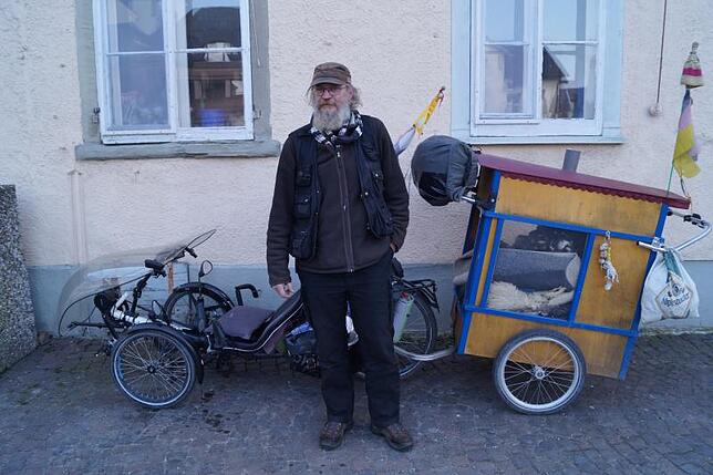 Mike steht vor seinem Fahrrad mit Anhänger, auf dem sein Hund schläft. Damit möchte er bald nach Norderney fahren.