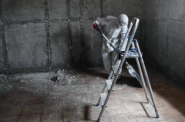 In einem Keller in Meckenbeuren arbeiten Handwerker in Schutzkleidung.