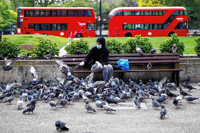 Ein Frau mit Maske füttert in London Tauben.