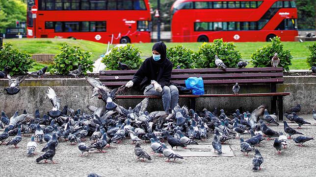 Ein Frau mit Maske füttert in London Tauben.