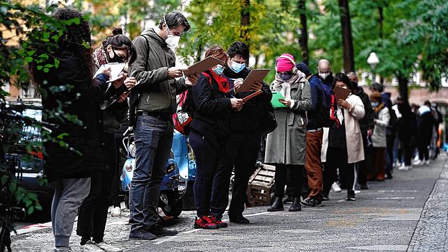 Menschen mit Mund- und Nasenschutz stehen in einer langen Schlange vor einer Arztpraxis im Berliner Bezirk Neukölln für einen ...